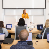 A professor teaches from the podium at the front of a classroom