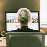 A woman with blonde hair sits in an office chair looking at a computer screen