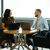 A professor and a student speak animatedly at a small round table inside of an office